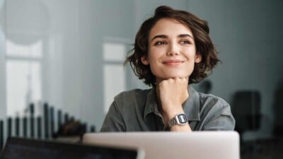 Young brunette woman smiling behind a laptop with her head resting on her hand