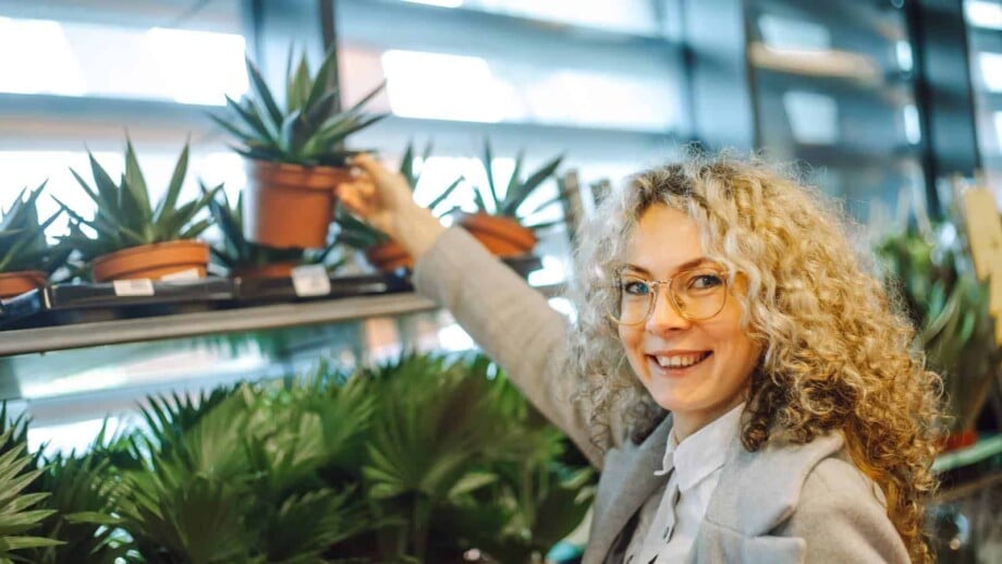 Blonde woman reaching for a potted succulent in a plant store