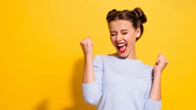 Young woman yelling in excitement in front of a yellow background