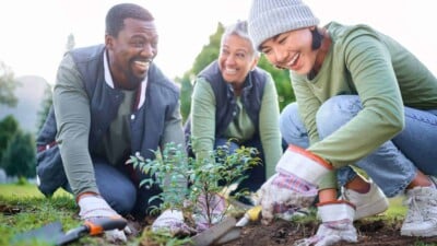 3 friends smiling while working together in a garden