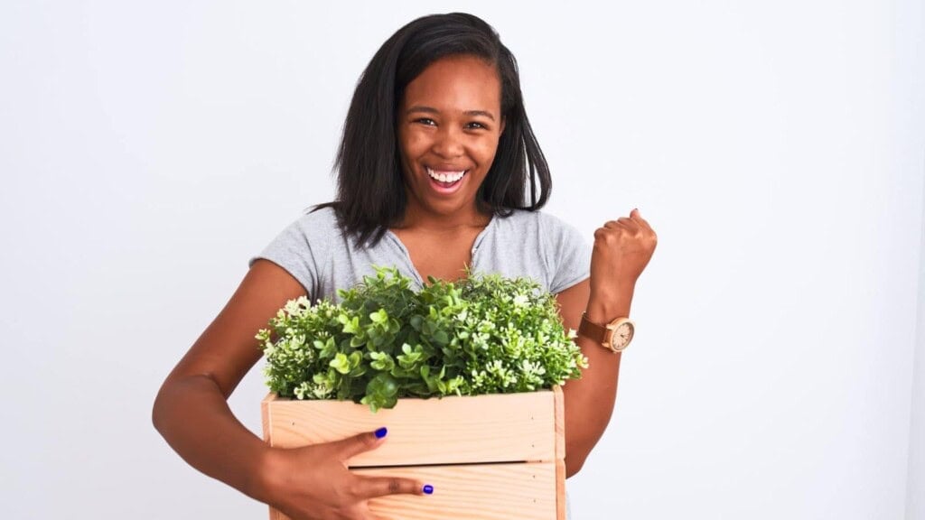 African american woman smiling and fist pumping while holding a plant in a basket.