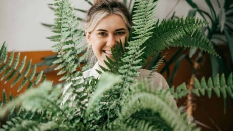 A young woman smiling and holding a potted fern