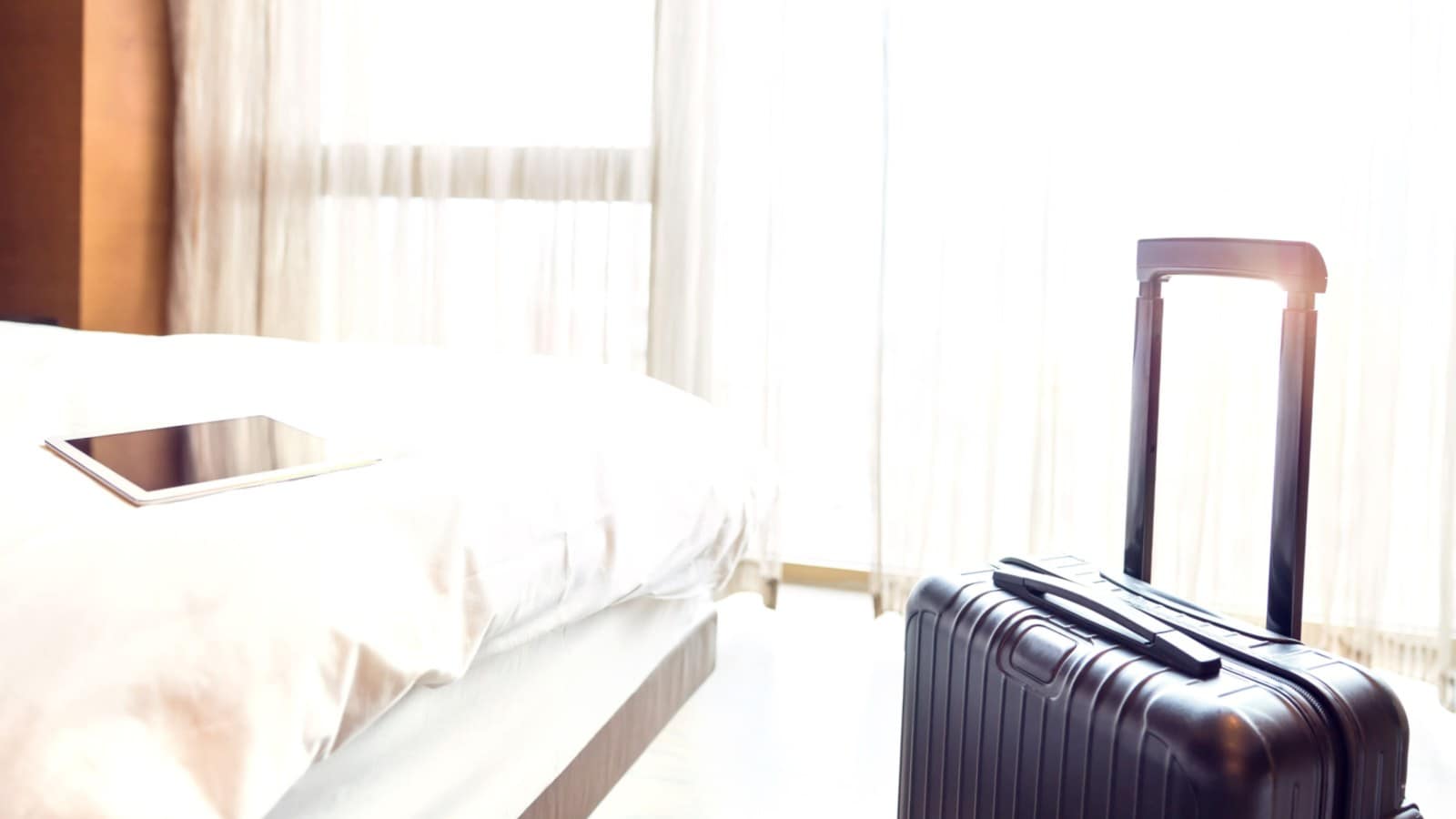 Black luggage on a hotel room with an iPad on the bed