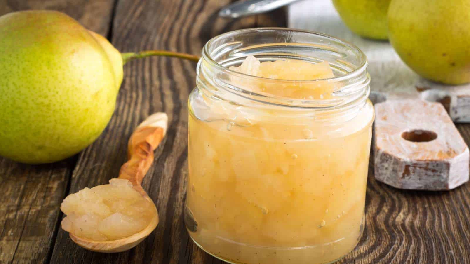 Homemade pear jam in a glass container with pear fruits on the table