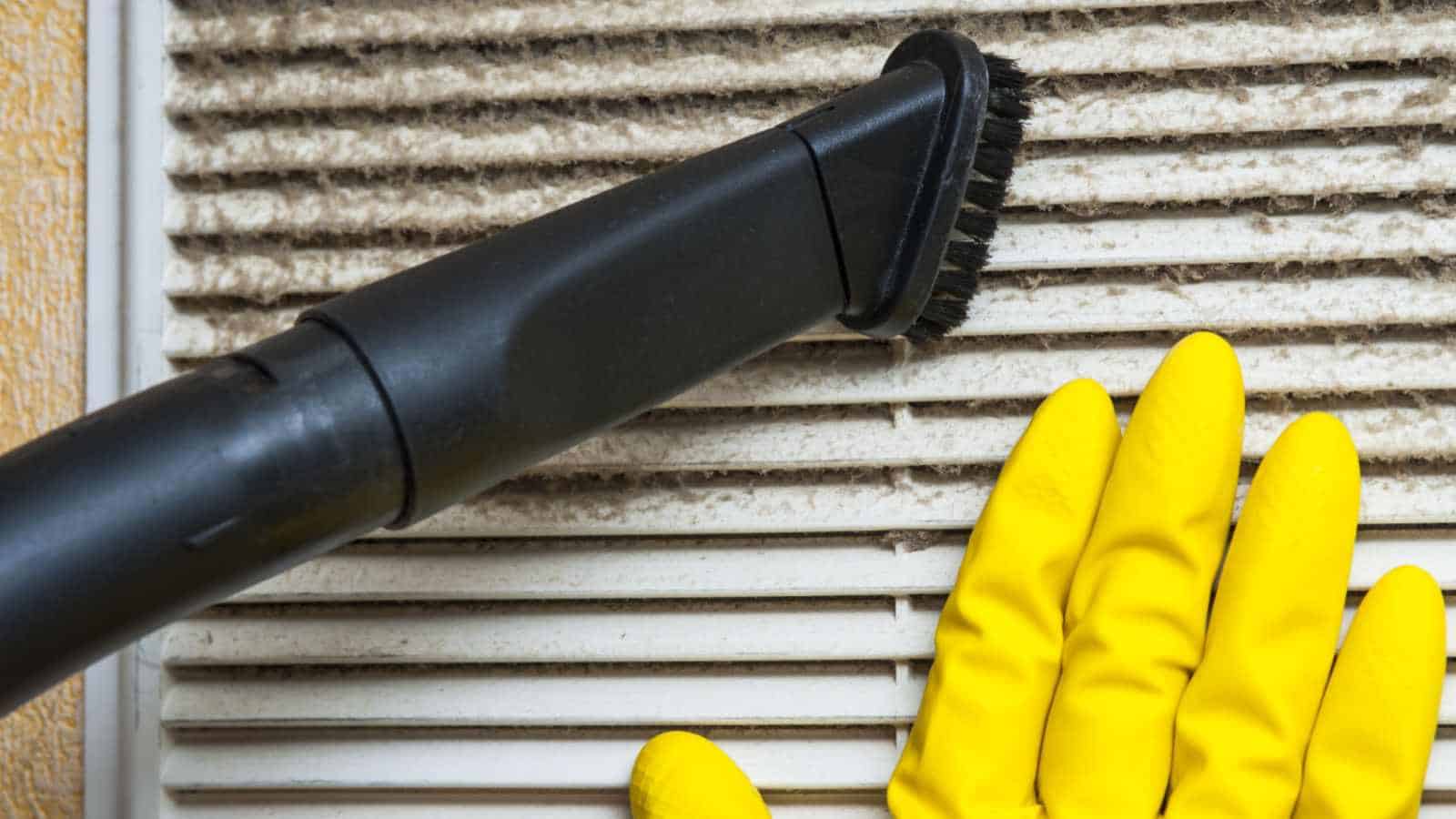 Man with yellow gloves vacuuming crevices of ventilation grills