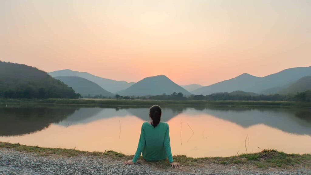 Woman sitting alone by the lake during sunset