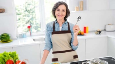 Mature lady holding soup spoon in kitchen