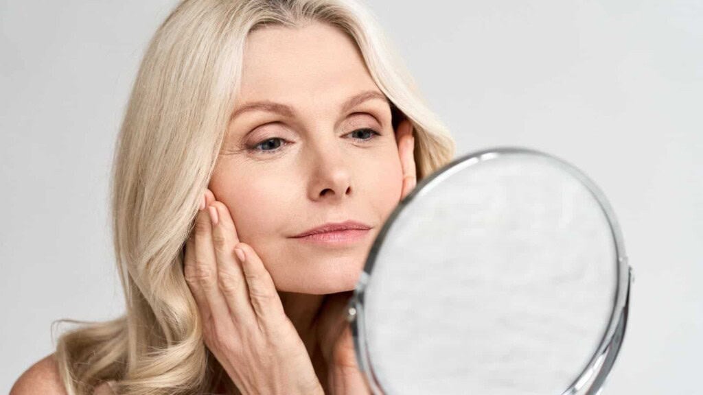 Happy middle aged woman looking at mirror touching her skin