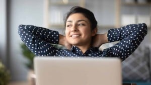 Young indian woman crossed hands behind head, enjoying break time at home behind laptop