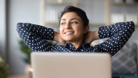 Young indian woman crossed hands behind head, enjoying break time at home behind laptop