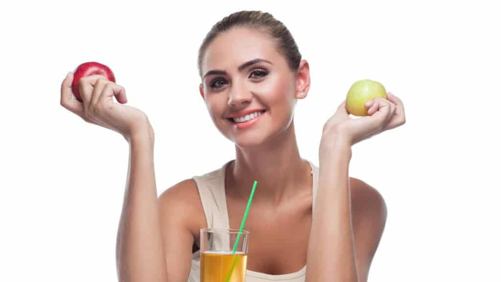Young woman, holding 2 apples and drinking apple cider vinegar.
